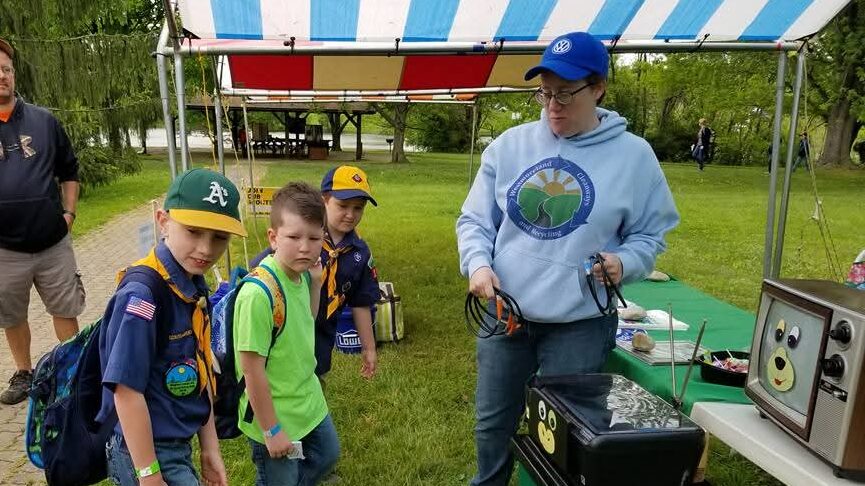 Staff member demonstrating recycling equipment to children at an outdoor community event.