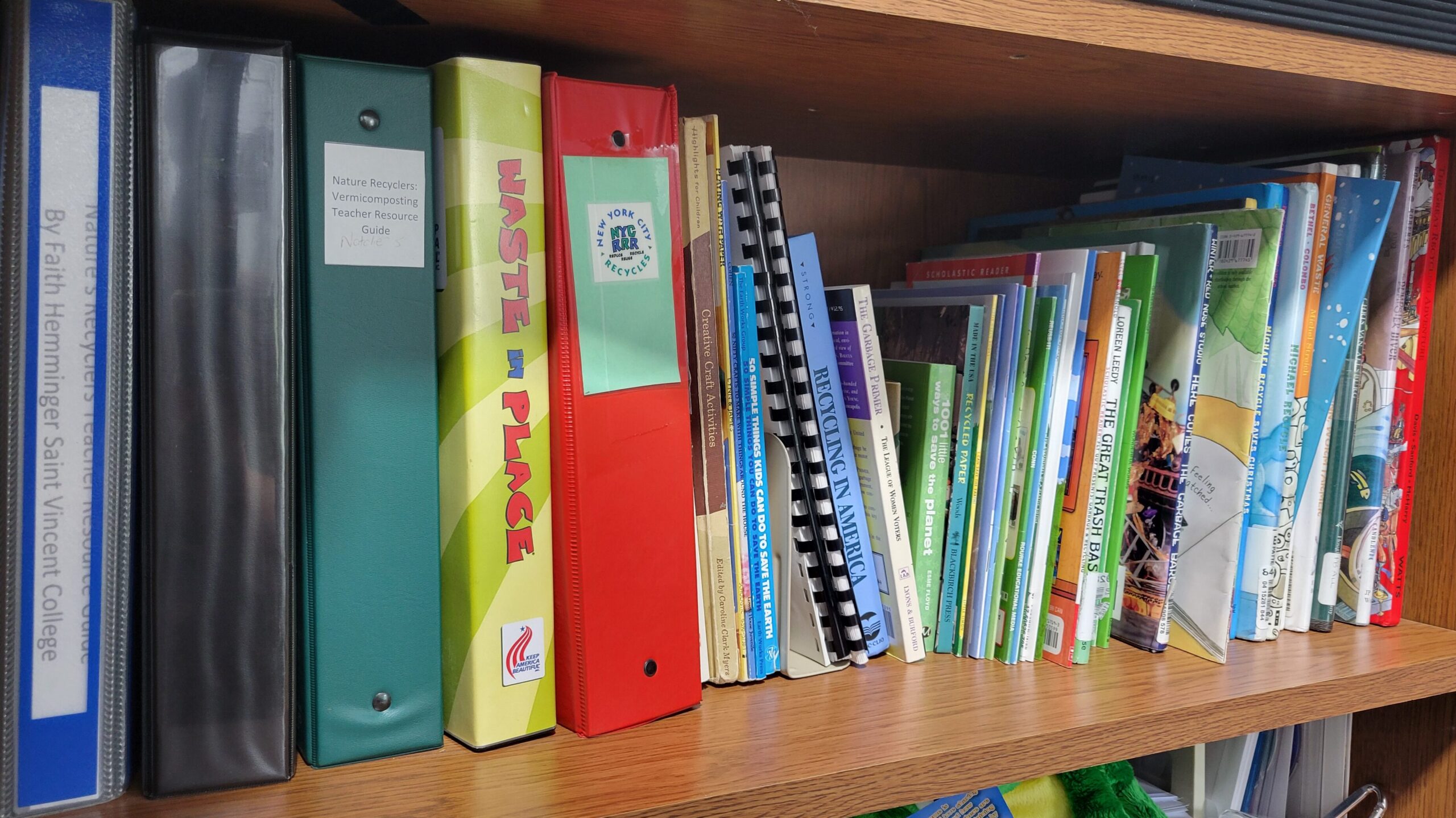 Shelf filled with environmental education binders, manuals, and resource books.